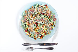 Frozen vegetables in a light plate and cutlery on a blue background.