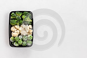 Frozen vegetables in a plastic container on a white background. Set of cabbage, broccoli, cauliflower, brussels sprouts. View from