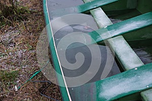 Frozen water in broken green boat on the bank of the river
