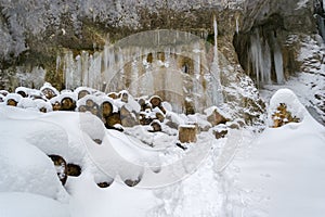 Frozen water columns on a rock wall, with wooden logs cut to size and covered in fresh snow