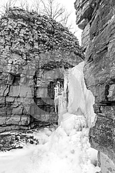 Frozen waterfall spilling out between two high natural layered r