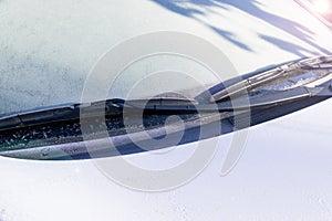 Frozen windshield wiper and glass on car. Frozen windshield. Frozen white car in winter. Ice on front window of a car