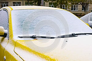 Frozen yellow car covered snow at winter day, view front window windshield and hood.