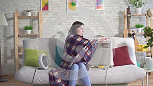 Frozen young woman in the living room and basking next to electric heaters