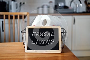 Frugal living, save money, live cheap concept with toilet paper basket and Frugal living text in frame on kitchen table