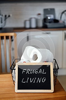 Frugal living, save money, live cheap concept with toilet paper basket and Frugal living text in frame on kitchen table