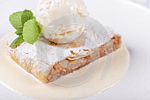 Fruit apple strudel cake served with ice cream, mint leaf and vanilla sauce. Classical austrian dessert on white plate
