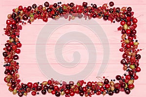 Fruit berries frame - redcurrants, gooseberries and blueberries on pink wooden background