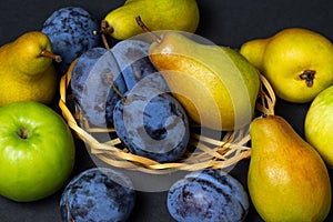 Fruit on a black background. Plums, pears and apples lie side by side.