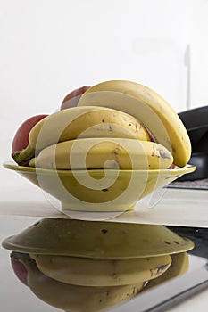 fruit bowl with bananas in the kitchen, next to the hot plate, we see its reflection in it