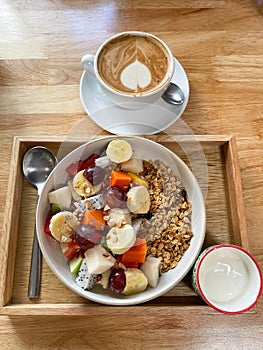 Fruit bowl with granola and yoghurt on wooden tray and coffee cup