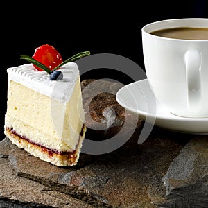 Fruit cake with cherries, grapes and plum stands on a wild stone next to a white cup of coffee with a foam