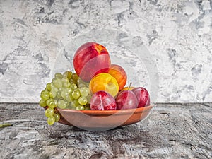 Fruit on a clay plate. Green grapes, nectarines and red plums