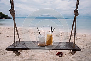 Fruit cocktails stand on a wooden swing overlooking a tropical beach. Healthy food