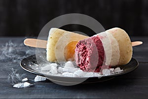 Fruit coffee homemade ice cream lolly on a stick in a black plate with slices of ice on a wooden dark table . Cold