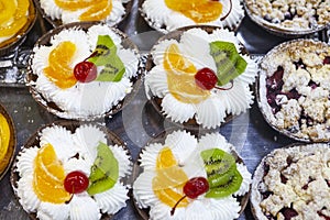 Fruit creamy cakes with canned cherry, orange and kiwi topping.