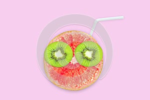 Fruit creative face with slices of grapefruit and kiwi, drinking straw on pink background, juice and summer concept