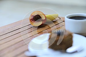 Fruit, a cup of coffee and a piece of chocolate cake on a wooden table.
