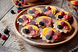 Fruit dessert tartlets with vanilla custard and fresh raspberries, blackberry, peach. Dark rustic style.