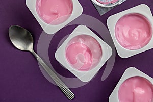 Fruit flavoured pink yogurt in white plastic cups on bright purple background with silver foil lid - Top view photo of yoghurt cup