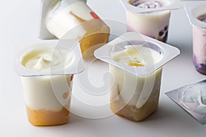 Fruit flavoured yogurt in transparent plastic cups on white background with silver foil lid - Yoghurt cups background with