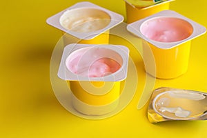 Fruit flavoured yogurt in yellow plastic cups on bright yellow background with silver foil lid in foreground photo
