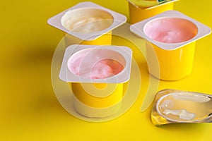 Fruit flavoured yogurt in yellow plastic cups on bright yellow background with silver foil lid in foreground