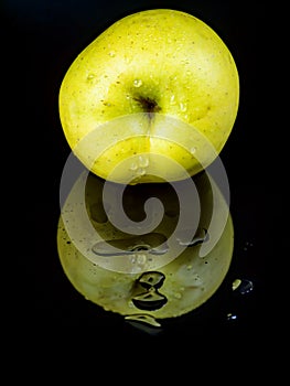 Fruit green apple in drops of water on a black glass background with reflection