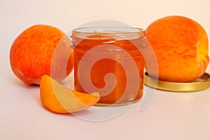 Fruit jam. Open glass jar with jam, sliced peaches and whole fruit on a light background. Concept of useful home stocks.