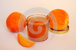 Fruit jam. Open glass jar with jam, sliced peaches and whole fruit on a light background. Concept of useful home stocks.