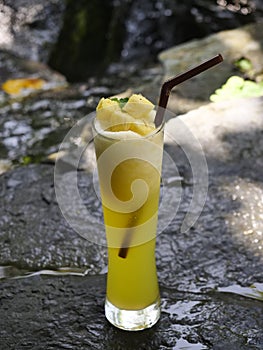 fruit juice, fruit smoothie, fruit juice, fruit juice in glass Placed on a rock near the waterfall