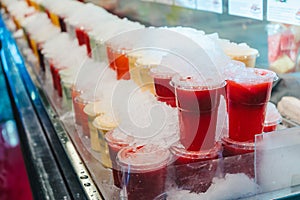 Fruit juice mix with ice arranged in plastic cups on a market stall with small fork inside, takeaway snack