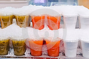 Fruit juice mix with ice arranged in plastic cups on a market stall with small fork inside, takeaway snack