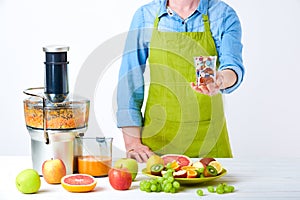 Fruit juice, pills and vitamin supplements. Woman holding glass full of pills standing next to juicer with loads of fresh fruit