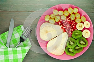 Fruit mix pear, kiwi, grapes, banana, pomegranate on a wooden background. fruit on a plate