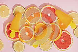 Fruit orange ice lolly and slices of orange, lime and grapefruit on pink background.