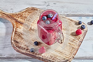 Fruit pink smoothie with berries in a glass jar on a wooden white table. Copy space