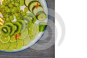 Fruit plate on table with grapes, kiwi, lime, pear and orange, sliced pieces on a white background, isolated