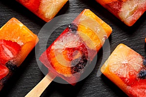 Fruit popsicles, homemade fruit ice lolly of various fruits with the addition of citrus lemonade on a black background, top view.