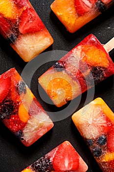 Fruit popsicles, homemade fruit ice lolly of various fruits with the addition of citrus lemonade on a black background, top view.