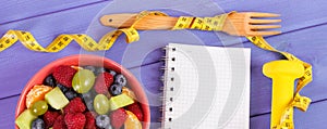 Fruit salad, centimeter with dumbbells and notepad for writing notes, healthy lifestyle and nutrition concept