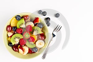 Fruit Salad in Green Bowl, blueberries and fork on white Table, Top View. copy space