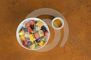 Fruit salad with honey in white bowl on stone background.