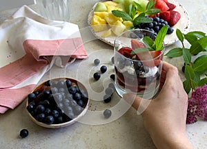 Fruit salad and natural greek yogurt with fresh berries. Hand holding glass with yogurt and fruits