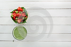 Fruit salad of strawberries, kiwi and pomegranate in a wicker basket and fresh green smoothies with lime and mint in a glass