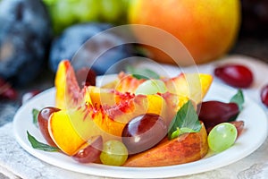 Fruit salad in white plate. Snack of fresh peaches, grapes, dogwood, plums, and mint leaves. Healthy Breakfast