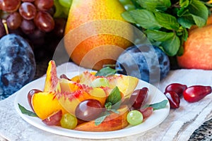 Fruit salad in white plate. Snack of fresh peaches, grapes, dogwood, plums, and mint leaves. Healthy Breakfast
