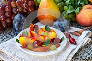 Fruit salad in white plate. Snack of fresh peaches, grapes, dogwood, plums, and mint leaves. Healthy Breakfast