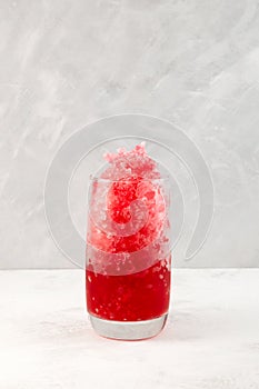 Fruit shaved ice in tall glass. Slushie - drink on grey background. Refreshing summer drink. Selective focus, copy space