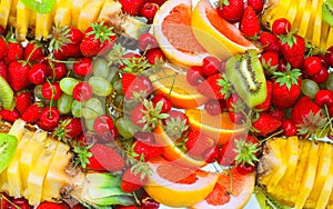 Fruit sliced oranges, banana, kiwi, cherries, grapefruit, strawberries, grapes and pineapple lying on a white plate